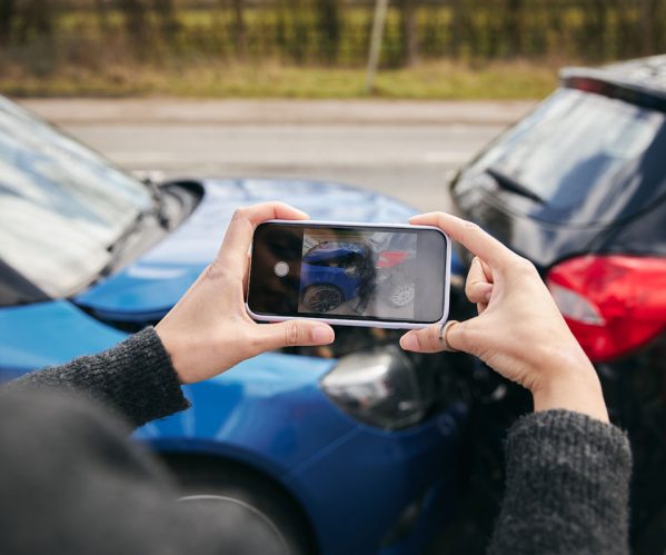 Close up of female driver taking photos of road traffic accident on mobile phone for insurance claim; Shutterstock ID 1964162257; purchase_order: -; job: -; client: -; other: -